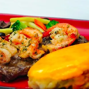 a steak, shrimp, and vegetables on a red plate