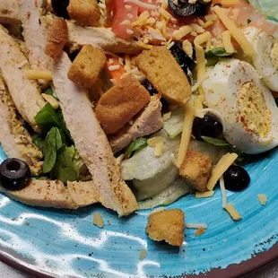 a salad with chicken, lettuce, olives, and cheese