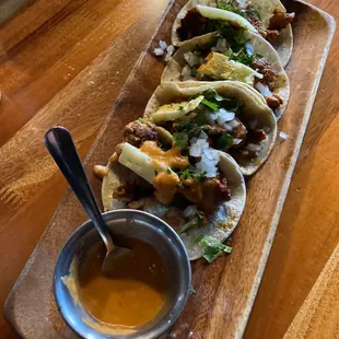 three tacos on a wooden platter with a small bowl of sauce