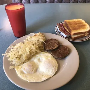 Two eggs medium, hash browns, patty sausage, white toast with strawberry jelly and a glass of orange juice.
