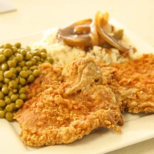 a plate of fried chicken, mashed potatoes, peas, and gravy