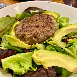 Grass fed beef burger on leafy greens with avocado