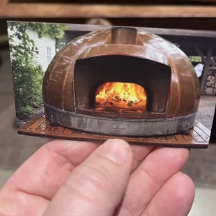 a hand holding a picture of a pizza oven