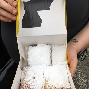 a person holding a box of beignets