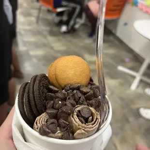 a hand holding a cup of ice cream with chocolate and cookies