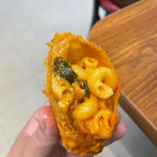 a hand holding a piece of macaroni and cheese