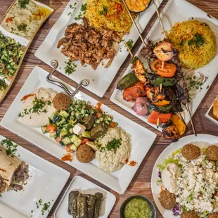 An appetizing spread of Mediterranean dishes, featuring colorful plates of grilled kebabs, rice, hummus, fresh salads, falafel wraps &amp; pita