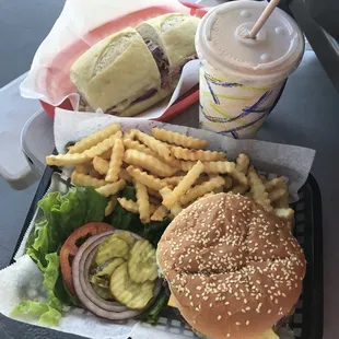 Pastrami sandwich in back and in front a chocolate milkshake, krinkle fries and a Avochee Burger