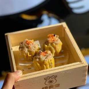 a person holding a small wooden box filled with dumplings