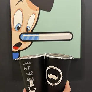 a hand holding two cups of coffee