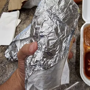 a hand holding a sandwich wrapped in aluminum foil