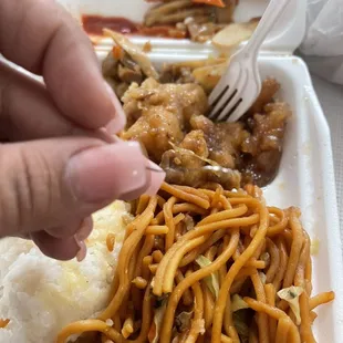 a hand holding a fork over a plate of noodles