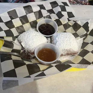 Beignets with powdered sugar with fudge and caramel on the side.