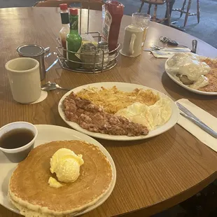 Corn beef hash with hash browns, eggs, and pancakes. And a biscuit with sausage and egg on it covered in gravy