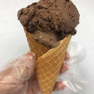 a hand holding a cone of chocolate ice cream