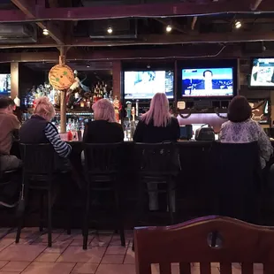 people sitting at a bar watching tvs