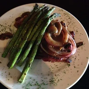 Cowboy Steak Hamburger patty wrapped in bacon topped with mushrooms and onions served over mashed potatoes with a side of grilled asparagus
