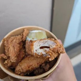 a hand holding a bowl of fried chicken