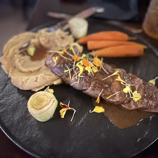 a steak and vegetables on a black plate