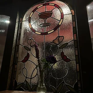 a vase of flowers in front of a stained glass window
