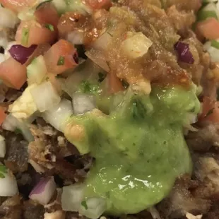 Carnitas and chicharron chopped up and mixed with all the salsas red, green, guacamole with pico de gallo and cilantro and onions