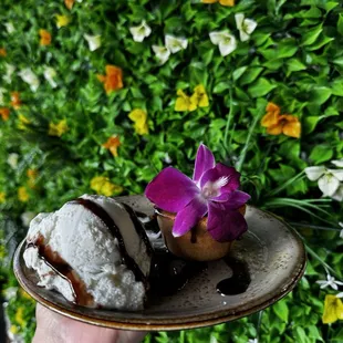 a hand holding a plate with ice cream and a flower