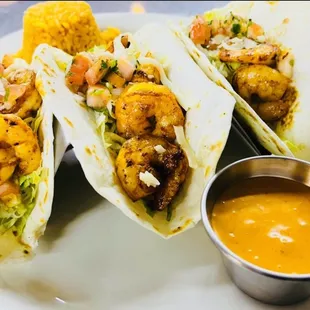 three tacos on a plate with a dipping sauce