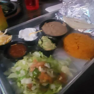 Sides of rice, beans, guacamole, sour cream, shredded cheese, lettuce and salsa