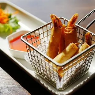 a basket of deep fried spring rolls with dipping sauce