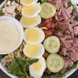 a salad with hard boiled eggs, ham, lettuce, tomatoes, cucumbers, and cheese