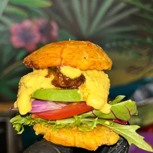 a hand holding a hamburger with cheese, lettuce, tomato, and onion