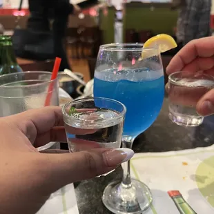 two people holding glasses of blue liquid