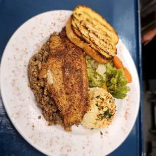 Blacked Catfish Entree-Blackened Catfish resting over a bed of Dirty Rice, served with potatoe salad, steamed veggies, and garlic bread.