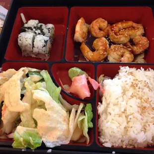 Lunch bento box with teriyaki shrimp, California roll, salad, and steamed rice.