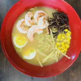 a bowl of ramen with shrimp, eggs, and corn