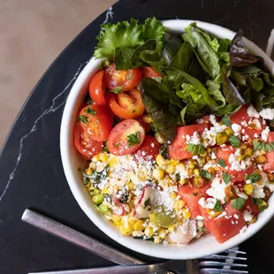 a bowl of salad with tomatoes, corn, lettuce, and feta cheese
