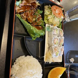 a bento lunch with rice, salad, and orange wedge