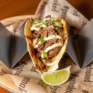 a taco with meat, cheese, onions, and a lime wedge