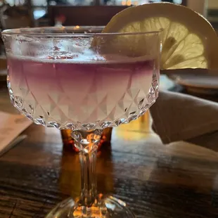 a purple cocktail with a slice of lemon on the rim