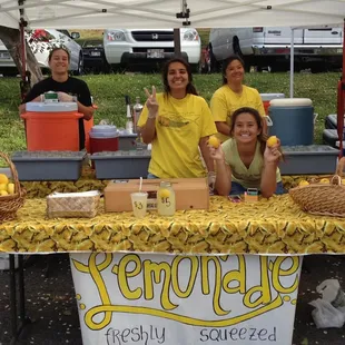  a group of people at a table with a sign that says lemonade freshly squeezed '