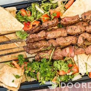 a tray of meat skewers with vegetables and pita chips