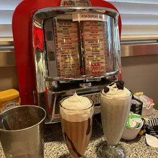 a soda machine and two glasses of milkshake