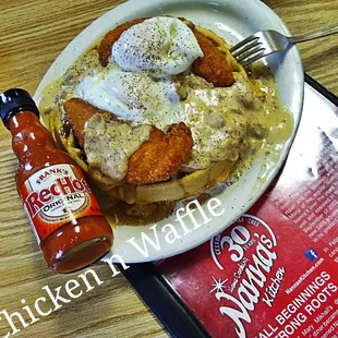 a plate of chicken waffle with sauce and a bottle of hot sauce
