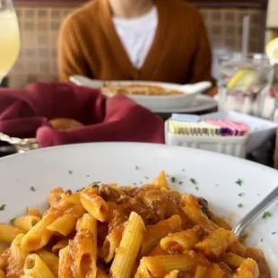 a woman sitting at a table with a plate of pasta and a glass of orange juice