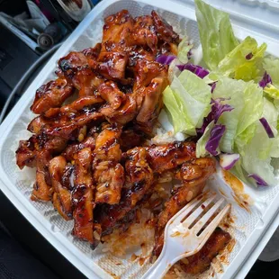 a plastic takeout container with chicken wings and lettuce