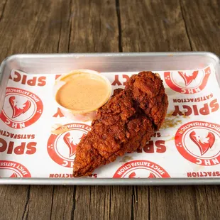 a fried chicken on a tray with a side of dipping sauce