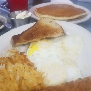 Two eggs over medium , hash browns, rye toast and one blueberry pancake.