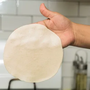 a person's hand holding an uncooked pizza crust