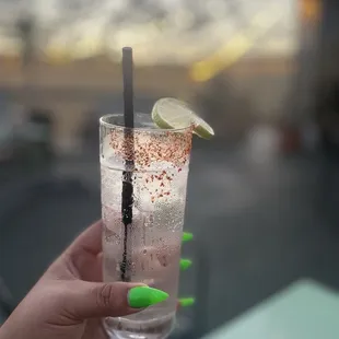a hand holding a tall glass of water with a lime slice on the rim