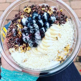 Acaí bowl with banana, blackberry, blueberry, granola, cacao nibs, coconut, and a coconut honey cream drizzle.